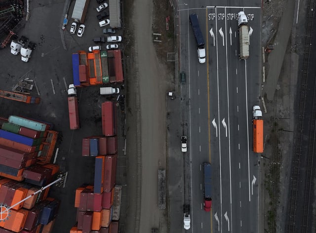 In an aerial view, trucks carrying shipping containers drive through the Port of Oakland.