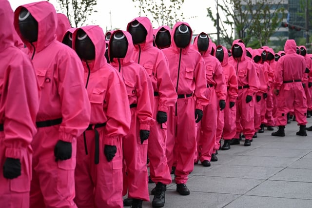 Les fans rassemblés près du palais  Gyeongbokgung à Séoul, avec des participants  vêtus des uniformes rose vif portés par les agents mystérieux et masqués de la série.