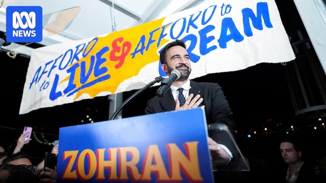 Mamdani stands below a sign that reads 'afford to live, afford to dream'