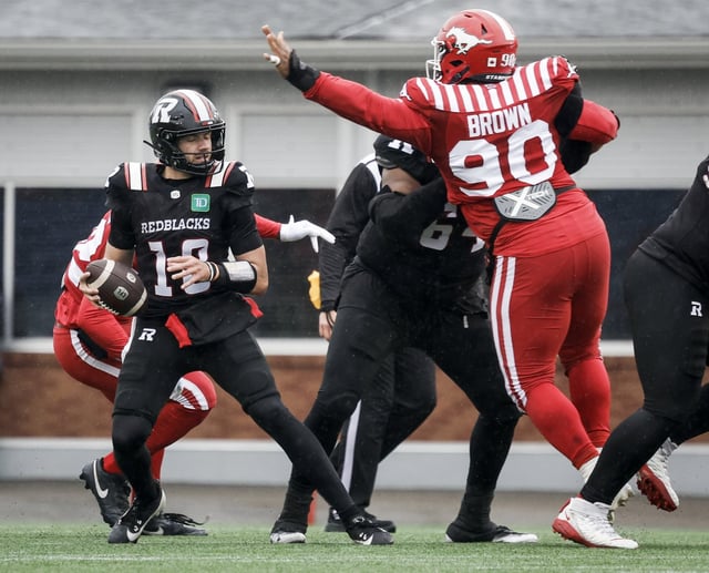 Ottawa Redblacks quarterback Dustin Crum, left, looks for a receiver as Calgary Stampeders' Miles Brown tries to block his pass during second half CFL football action in Calgary, Saturday, June 21, 2025.THE CANADIAN PRESS/Jeff McIntosh