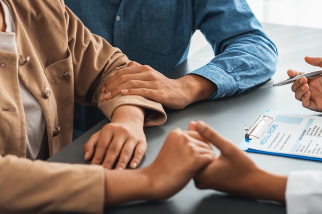 Doctor providing compassionate healthcare consultation while young couple patient holding hand, comfort each other after infertile report.