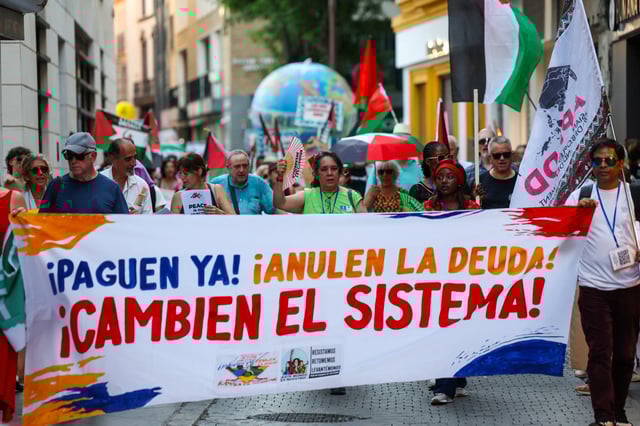 People carry a banner that reads ''Pay now! Cancel the debt! Change the system!'' as they take part in a march demanding a UN-led framework for sovereign debt resolution, on the eve of the 4th International Conference on Financing for Development, in Seville, Spain, June 29, 2025. REUTERS/Claudia Greco