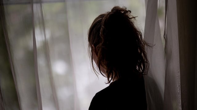 Eine Frau steht im Halbdunklen an einem Fenster
