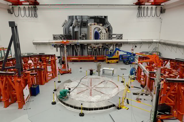 A person works on the cryostat base of the fusion reactor inside the tokamak hall at Commonwealth Fusion Systems in Devens, Massachusetts, on April 10. A full-sized image of the tokamak is superimposed onto the wall.