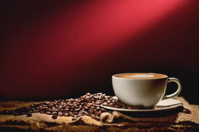 A cup of coffee paced on a table with coffee beans in the background