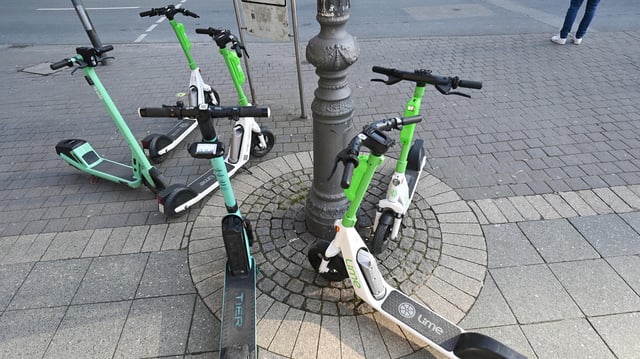 E-Scooter verschiedener Anbieter stehen in Frankfurt/Main um einen Lichtmasten herum.