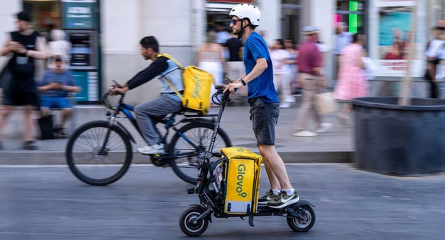Dos repartidors de Glovo, un en bicicleta i un altre en patinet, entreguen les seves comandes a Barcelona. | ZOWY VOETEN