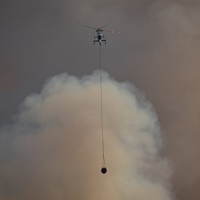 A helicopter with a water bucket flies past smoke rising into the air while battling the July Mountain wildfire along the Coquihalla Highway south of Merritt, B.C., on August 11, 2021. THE CANADIAN PRESS/Darryl Dyck