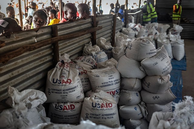 Congolese refugees look through a corrugated metal fence at the final batches of food delivered by the now-dismantled United States Agency for International Development (USAID) in a storage and food delivery area at the Musenyi refugee site in Giharo, on May 7.
