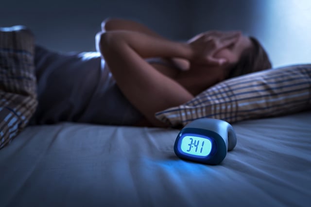 A stock image of a woman lying in bed struggling to sleep.