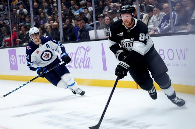 Kings defenseman Vladislav Gavrikov, right, controls the puck past Winnipeg Jets center Mark Scheifele during the first period of an NHL hockey game Wednesday, Nov. 27, 2024, in Los Angeles. (AP Photo/Ryan Sun)