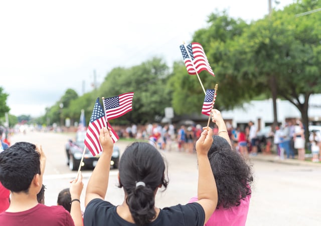 Rear view diverse people waving American flags watching street parade on July 4th Independence Day celebration. United and patriotism concept.
