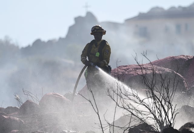 PERRIS, CALIFORNIA – JUNE 30: A firefighter sprays water as the Juniper Fire burns on June 30, 2025 near Perris, California. Dry conditions and hot temperatures are helping fuel multiple wildfires burning in Southern California after a rainy season which was below average. (Photo by Mario Tama/Getty Images)