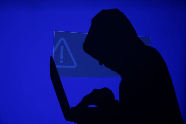 A hooded man holds a laptop computer as blue screen with an exclamation mark is projected on him in this illustration picture taken on May 13, 2017. REUTERS/Kacper Pempel/Illustration/ File Photo
