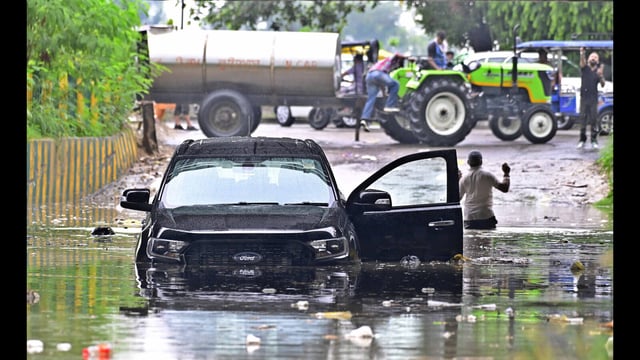 A person wading through water after his car was partially submerged at a waterlogged area near Chandar Nagar in Ludhiana on Tuesday. (Gurpreet Singh/HT)