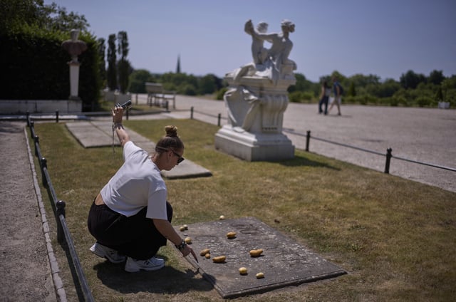 A woman takes a photo of herself as she places a potato on the grave stone of King Frederick II of Prussia, in the park of Sanssouci Palace in Potsdam, Germany, June 17, 2025. (AP Photo/Markus Schreiber)
