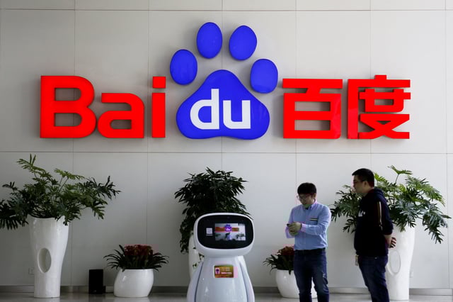 Men interact with a Baidu AI robot near the company logo at its headquarters in Beijing, China April 23, 2021. REUTERS/Florence Lo/File Photo