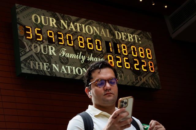 A man looks at his phone as he passes by the National Debt Clock in New York City, U.S., July 1, 2025.  REUTERS/Brendan McDermid