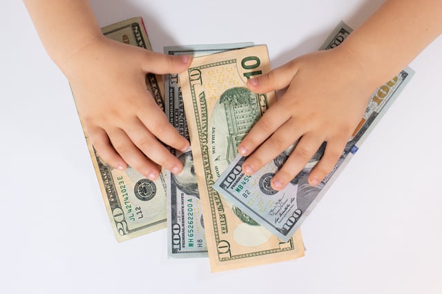 Stock image/file photo: A child&#39;s hands touching several U.S. Dollar bills.
