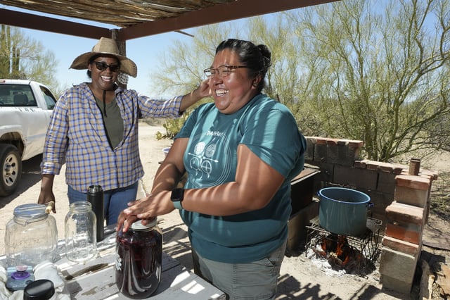 Maria Francisco, right, and Tanisha Tucker Lohse laugh as they cook and can saguaro cactus fruit on a harvest day for the Tohono Oʼodham people in Saguaro National Park near Tucson, Ariz., on Monday, June 23, 2025. (AP Photo/Ross D. Franklin)