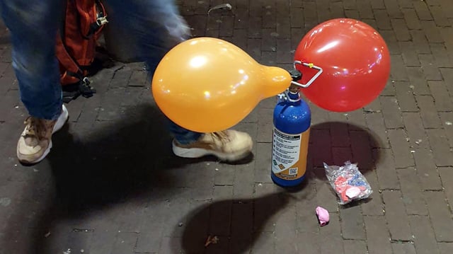 Lachgasflasche mit zwei aufgepumpten Luftballons.