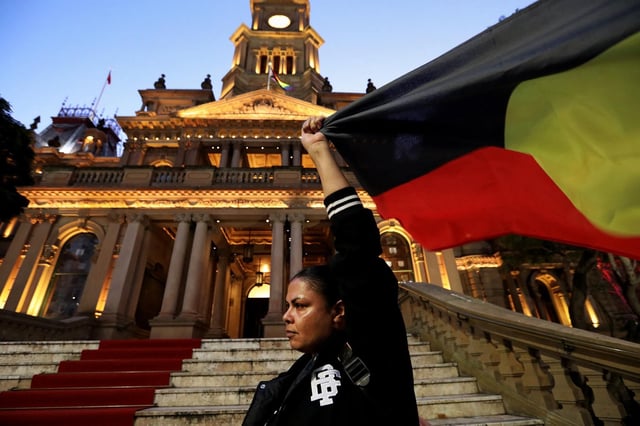 La commission Yoorrook, a présenté mardi 1er juillet 2025 au Parlement australien, son rapport sur la colonisation britannique, qui conclut à un génocide. (Photo : une femme tient le drapeau aborigène devant l’hôtel de ville de Sydney, le 7 juin 2025)