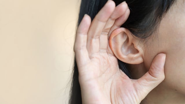 A woman holding her ear, trying to hear.
