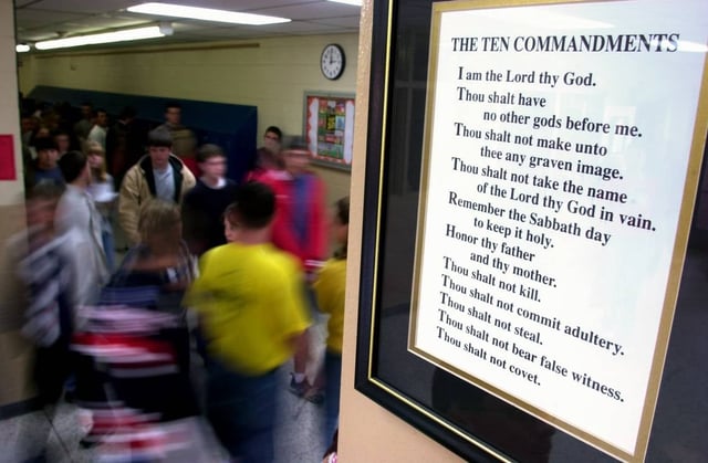 High school students walk through a hallway as a sign displaying the Christian "10 Commandments" is affixed to the glass window of a door