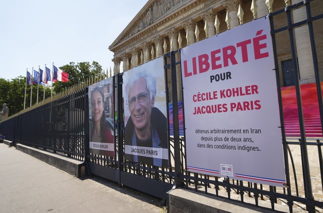 The portraits of French nationals Cecile Kohler, 40, left, and Jacques Paris, 72, imprisoned for more than 3 years in Iran are seen set up in front of the French National Assembly, in Paris, Thursday, July 3, 2025. (AP Photo/Aurelien Morissard)