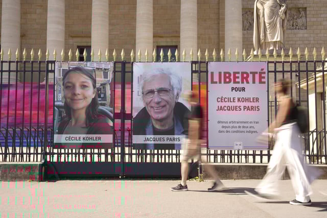 People walk past the portraits of French nationals Cecile Kohler, 40, left, and Jacques Paris, 72, imprisoned for more than 3 years in Iran set up in front of the French National Assembly in Paris, Thursday, July 3, 2025. (AP Photo/Aurelien Morissard)