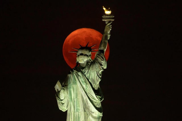 The full Buck Moon rising behind the Statue of Liberty on July 21, 2024.