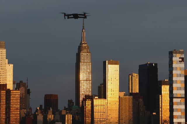 A drone flies in front of the skyline of midtown Manhattan and the Empire State Building as the sun sets in New York City.