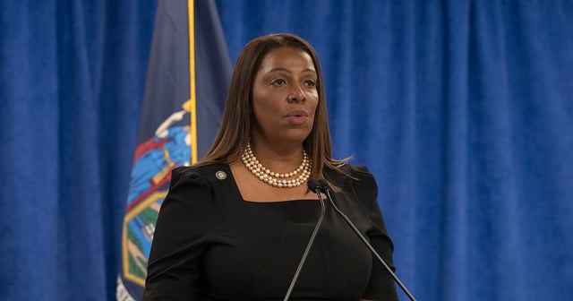 A Black woman stands behind a podium and in front of a large blue background and a New York State flag.