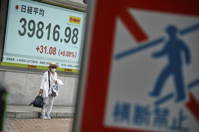 A person seen behind a traffic sign stands in front of an electronic stock board showing Japan's Nikkei index at a securities firm Friday, July 4, 2025, in Tokyo. (AP Photo/Eugene Hoshiko)