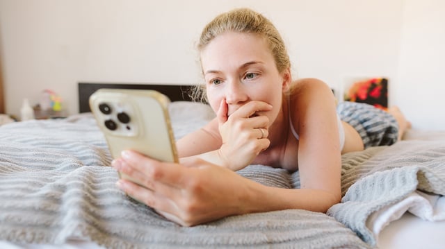 Frau in Unterwäsche guckt erschrocken auf ihr iPhone