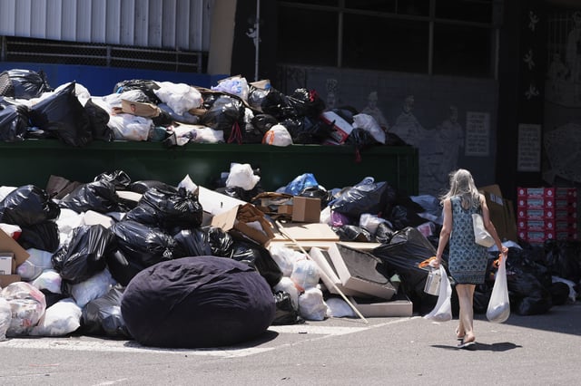 A woman drops off trash at a garbage collection site, Thursday, July 3, 2025, in Philadelphia. (AP Photo/Matt Slocum)