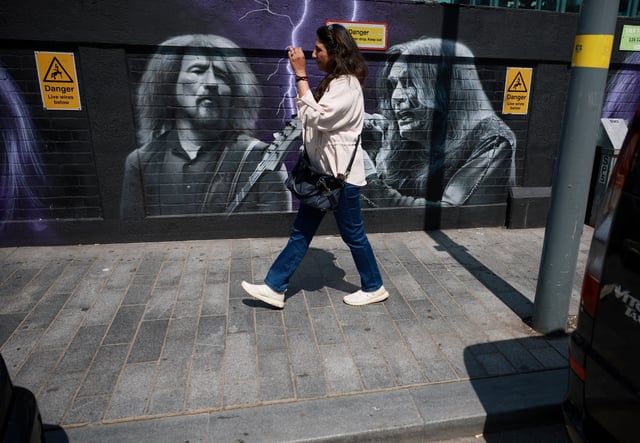 A woman walks past a mural painted in honour of rock band Black Sabbath ahead of their upcoming concert in Birmingham, Britain, July 2, 2025. REUTERS/Phil Noble/File Photo