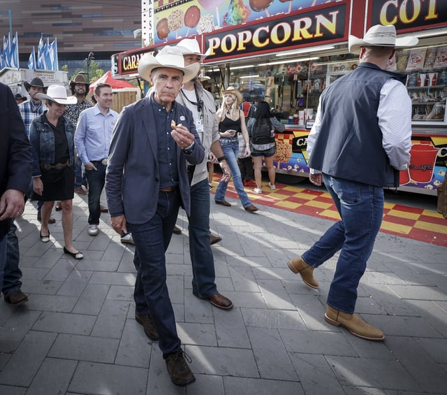 Prime Minister Mark Carney, centre, samples mini doughnuts as he walks through the Calgary Stampede grounds in Calgary, Alta., Friday, July 4, 2025.THE CANADIAN PRESS/Jeff McIntosh