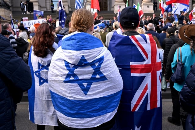 Des gens enveloppés du  drapeau australien et israélien lors d'un rassemblement à Melbourne après une tentative d'incendie visant une synagogue dans la ville, le 6 juillet 2025