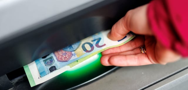 Eine Frau nimmt Geldscheine aus einem Geldautomaten entgegen