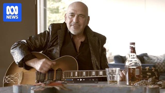 A man wearing a leather jacket and playing guitar at a table