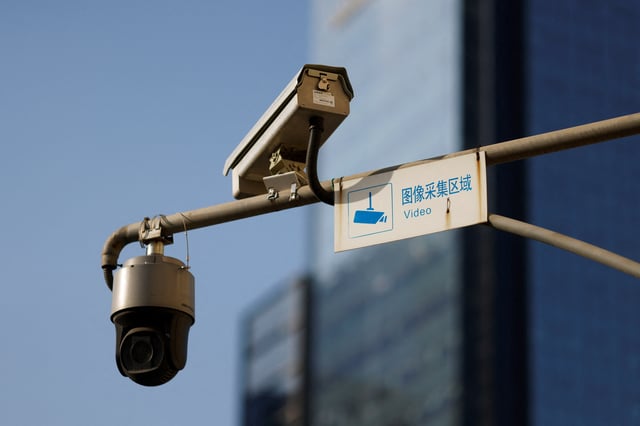 A video surveillance sign is seen next to Hikvision surveillance cameras overlooking a street in Beijing, China December 14, 2021. REUTERS/Carlos Garcia Rawlins/File Photo