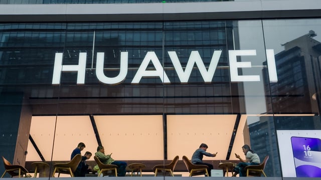 huawei logo on a building with people sitting in an office reception setting.