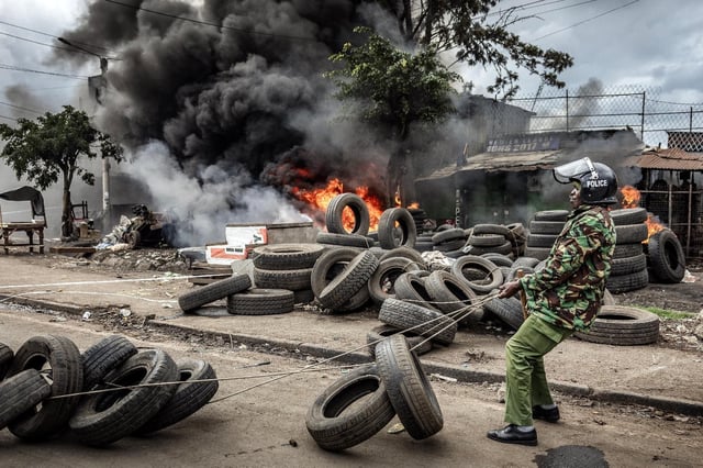 Un policier kényan déplace des pneus bloquant un axe routier, le 7 juillet 2025 à Nairobi.