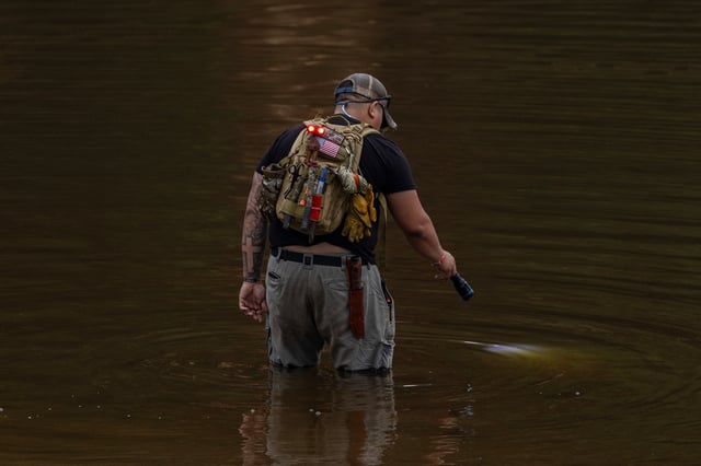 A search and recovery worker shines his flashlight through through murky waters near Camp Mystic, looking for remains of victims on July 6, 2025 in Hunt, Texas. 