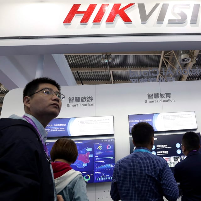 In this Tuesday, Oct. 23, 2018, file photo, visitors pass by a booth for state-owned surveillance equipment manufacturer Hikvision at the Security China 2018 expo in Beijing, China. (AP Photo/Ng Han Guan, File)