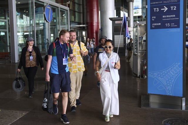 A tour guide leads tourists to the shutter bus to take a half-day tour to the tourism destination which offered by a travel agency Trip.com Group, at the Beijing Capital International Airport, in Beijing on June 15, 2025. (AP Photo/Andy Wong)