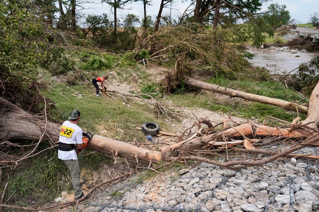 Hayley Bosworth, al fondo, y Simon Ball, a la izquierda en primer plano, cortan ramas de árboles durante labores de limpieza luego de una inundación, el lunes, en Center Point, Texas. (AP/Ashley Landis)