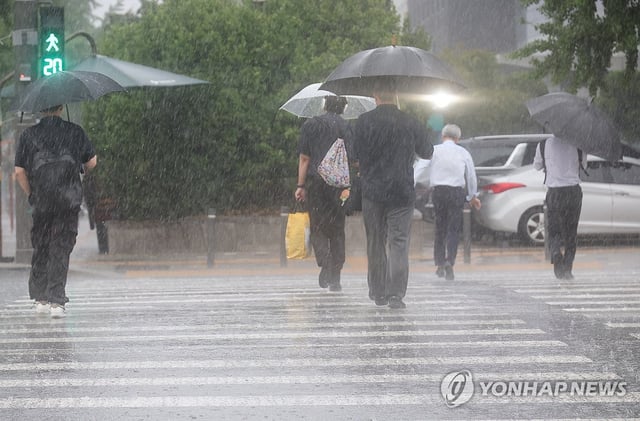 People cross a crosswalk with umbrellas near the National Assembly in Seoul as a sudden downpour hits the area during the evening commute hours on July 8, 2025. (Yonhap)