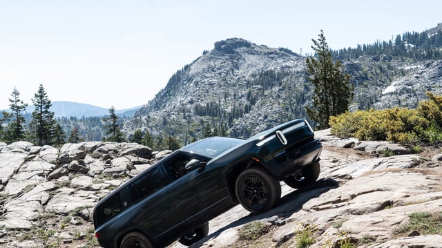 A blue Rivian R1S drives up a 45-degree rock slope.